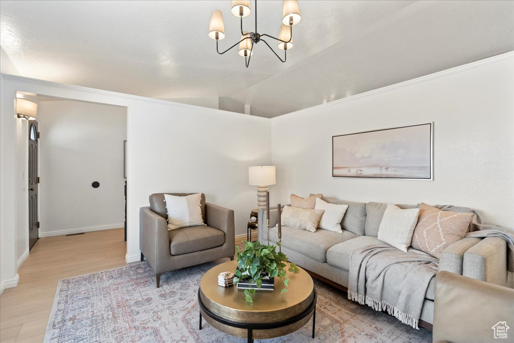 Living room featuring a chandelier, wood-type flooring, vaulted ceiling, and crown molding