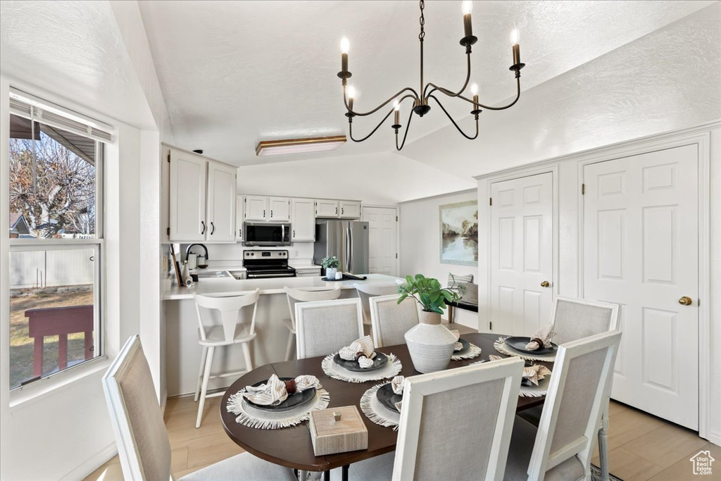 Dining area with light hardwood / wood-style flooring, an inviting chandelier, lofted ceiling, and sink