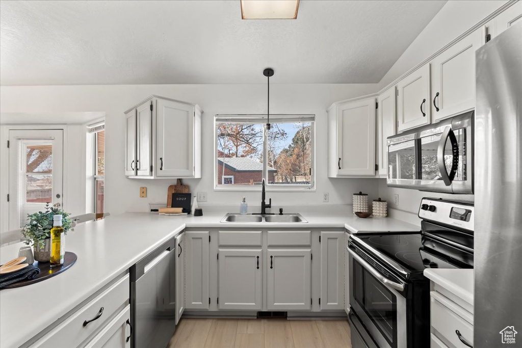 Kitchen with white cabinets, appliances with stainless steel finishes, hanging light fixtures, and sink