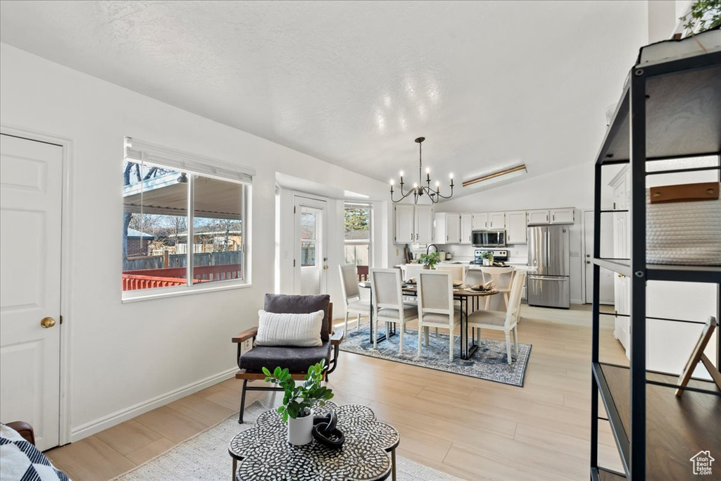 Dining room featuring a notable chandelier, light hardwood / wood-style floors, a textured ceiling, and vaulted ceiling