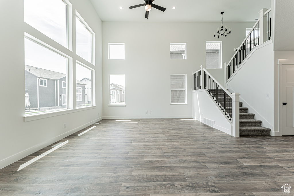 Unfurnished living room with stairs, healthy amount of natural light, a chandelier, a ceiling fan, and a high ceiling