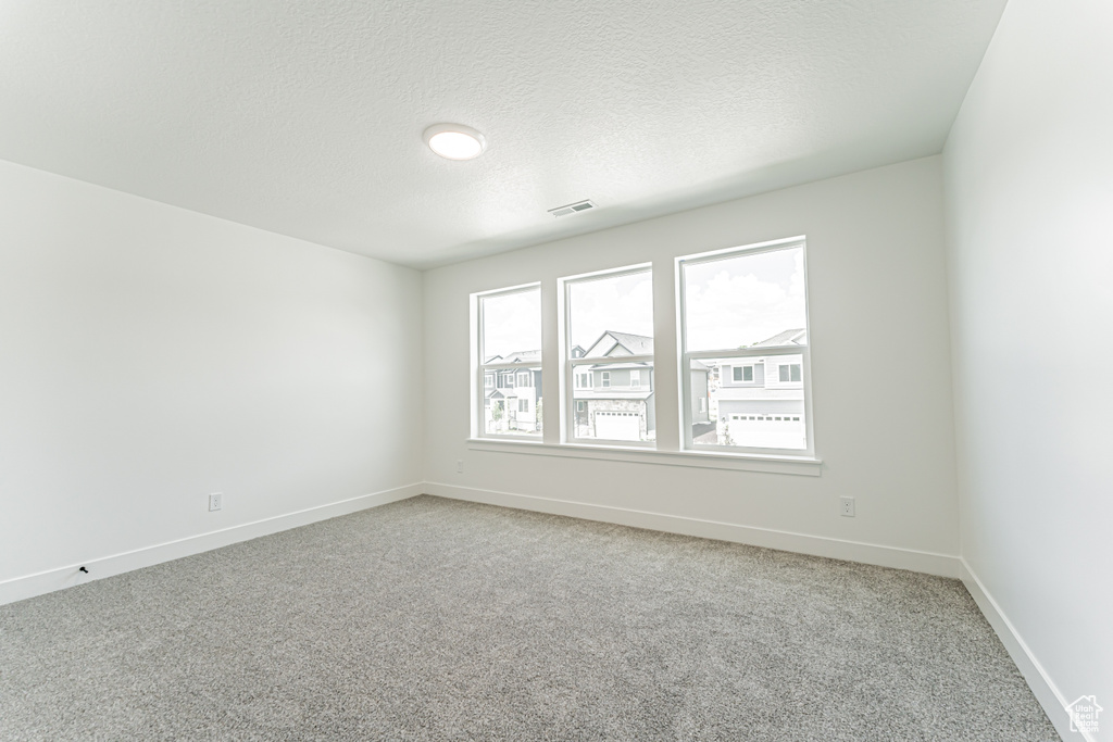 Unfurnished room featuring light colored carpet, baseboards, and a textured ceiling