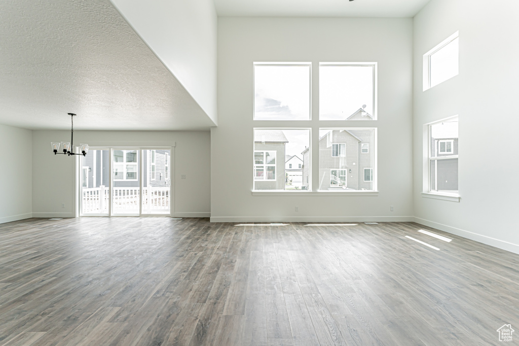 Unfurnished living room featuring a chandelier, wood finished floors, healthy amount of natural light, a towering ceiling, and baseboards