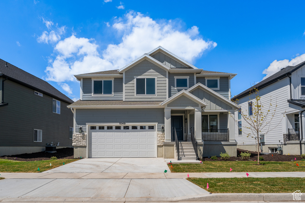 Craftsman inspired home featuring board and batten siding, driveway, an attached garage, a porch, and cooling unit