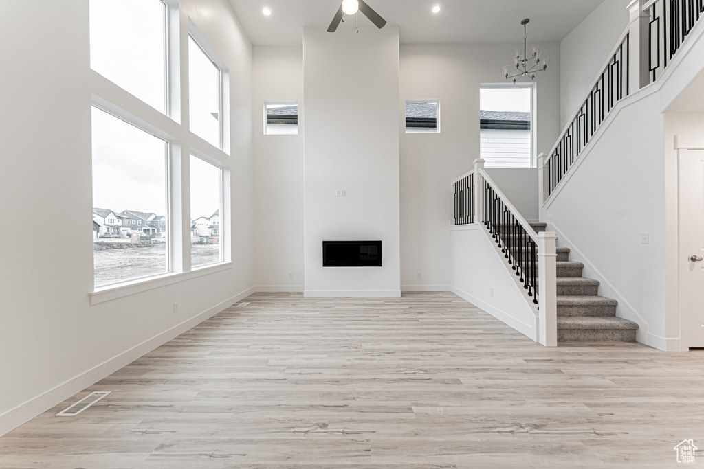 Unfurnished living room with visible vents, baseboards, a high ceiling, stairs, and light wood-style floors