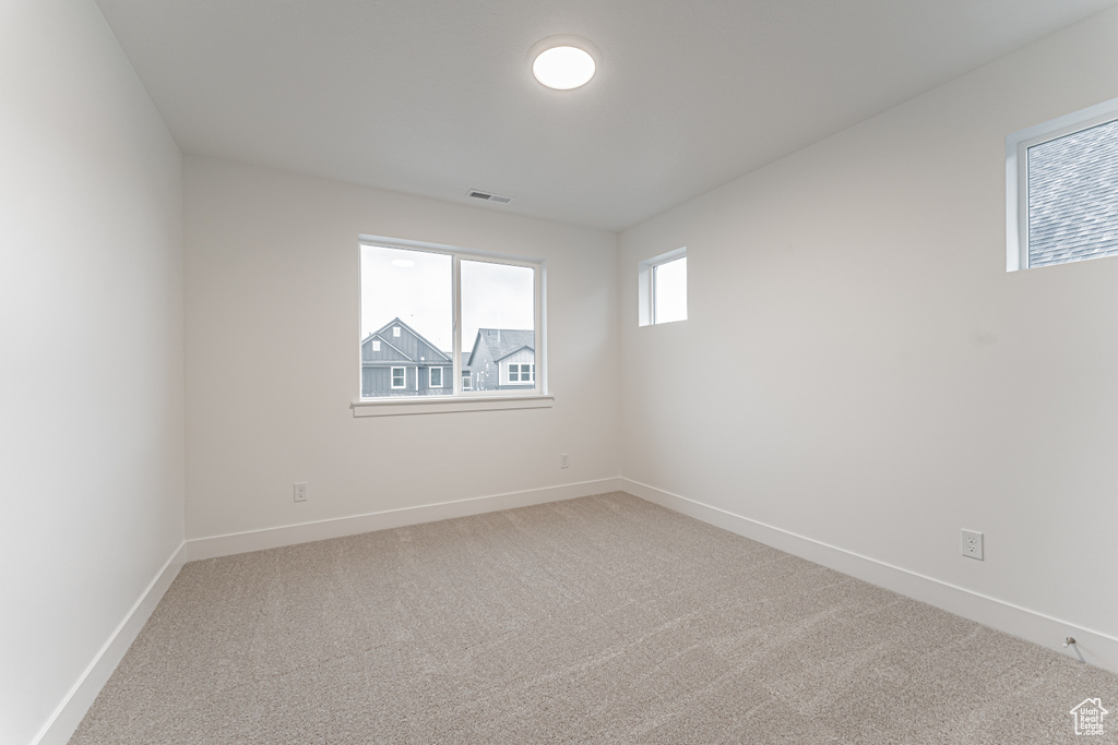 Empty room featuring visible vents, light colored carpet, and baseboards