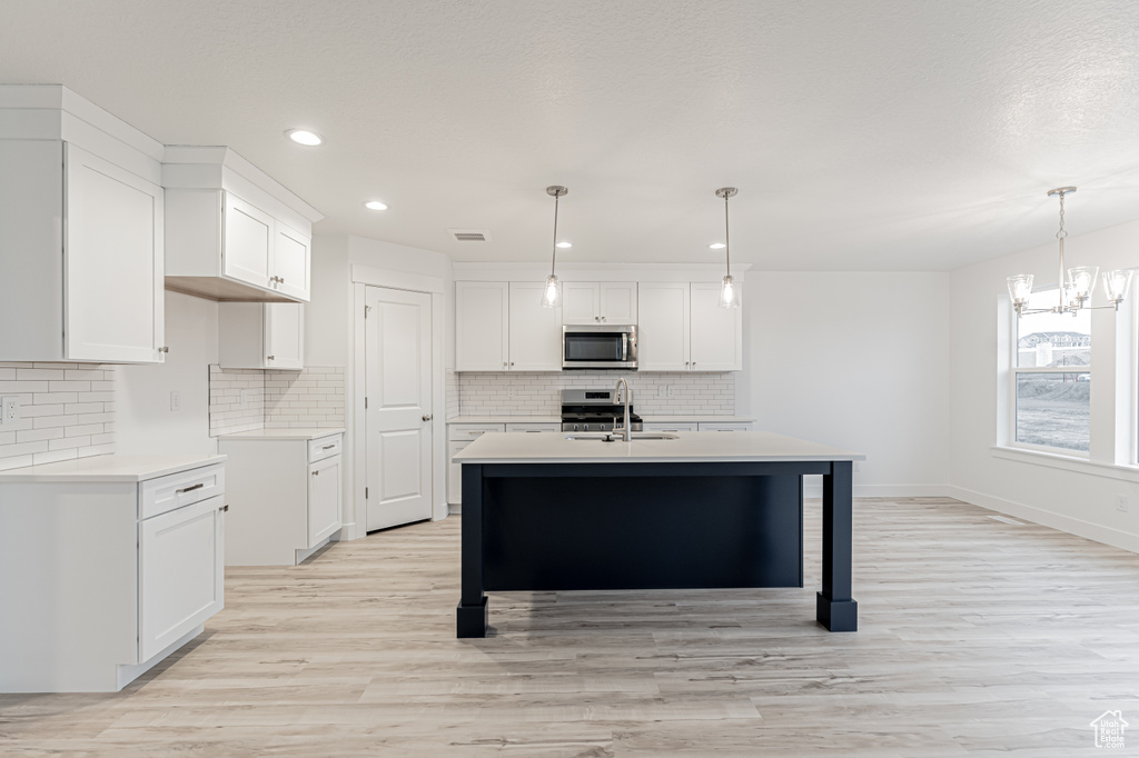 Kitchen with stainless steel microwave, an island with sink, a notable chandelier, white cabinets, and a sink