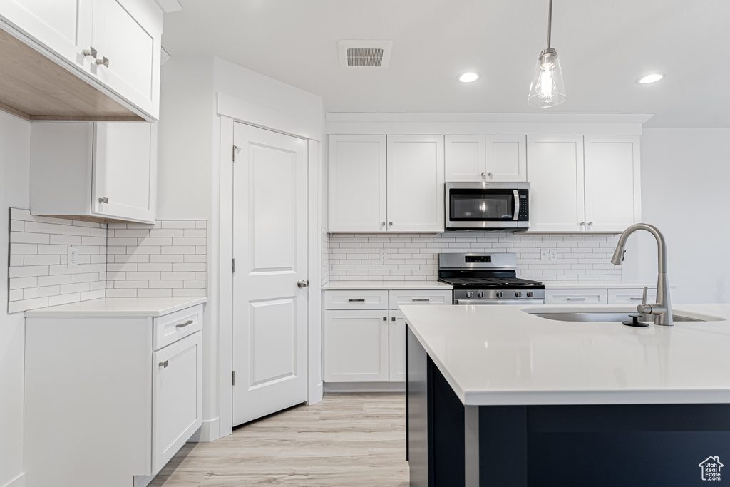 Kitchen featuring light countertops, light wood-style flooring, hanging light fixtures, stainless steel appliances, and a sink