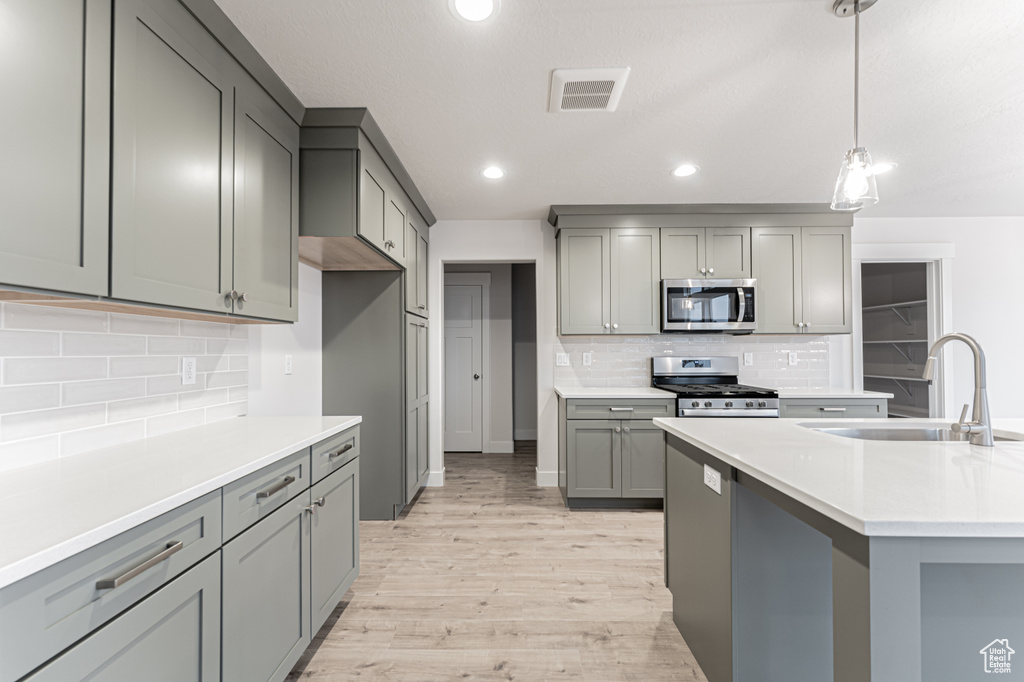 Kitchen with pendant lighting, light wood-type flooring, gray cabinets, appliances with stainless steel finishes, and a sink