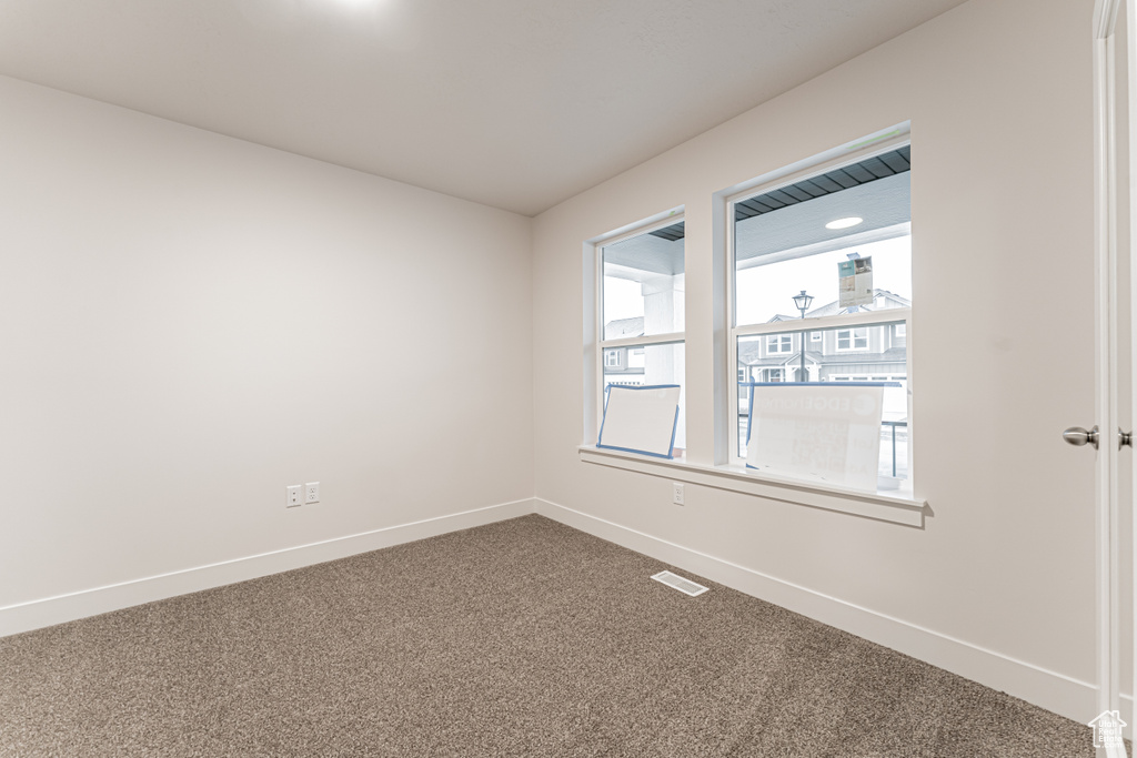 Spare room featuring visible vents, baseboards, and dark carpet