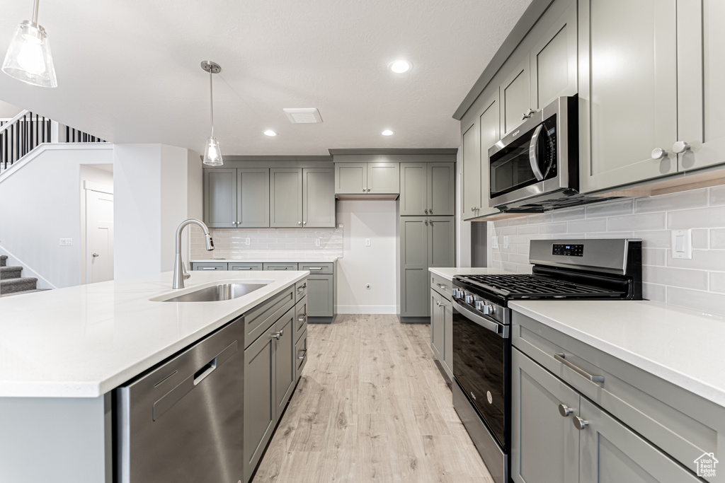 Kitchen featuring light wood-style flooring, gray cabinets, a sink, stainless steel appliances, and light countertops