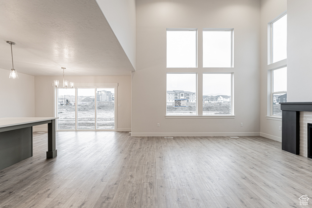 Unfurnished living room featuring baseboards, light wood-style floors, a tile fireplace, and a chandelier
