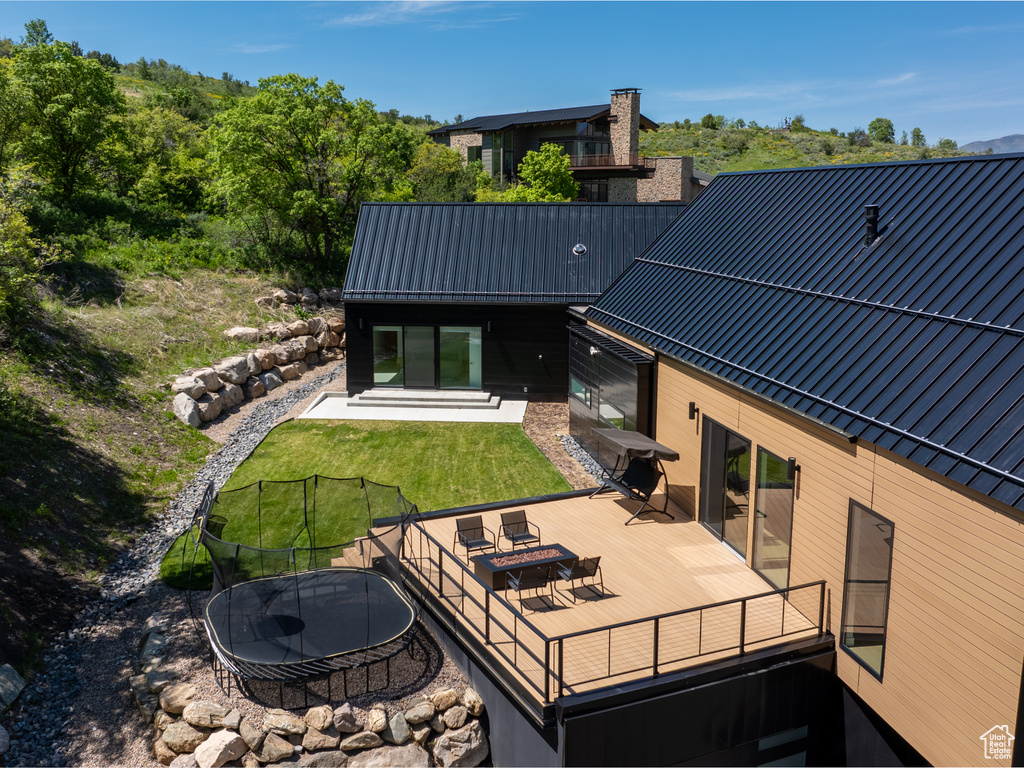 Rear view of property featuring a wooden deck, a lawn, metal roof, and a trampoline