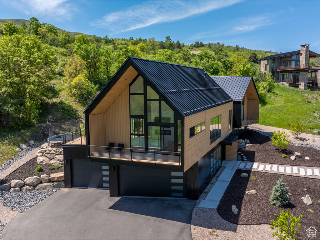 Contemporary home with a garage, a balcony, asphalt driveway, metal roof, and a view of trees