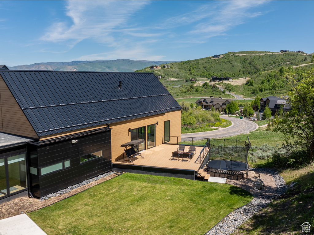 Back of house with a trampoline, a deck with mountain view, and a lawn