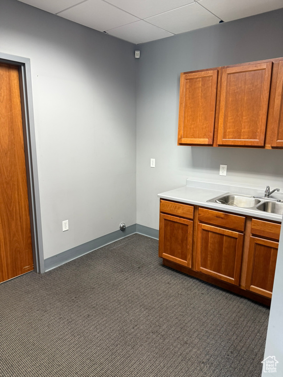 Kitchen featuring brown cabinets, a sink, light countertops, dark colored carpet, and baseboards