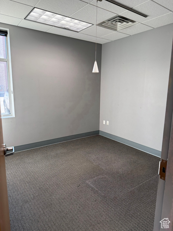 Carpeted empty room with baseboards, visible vents, and a drop ceiling