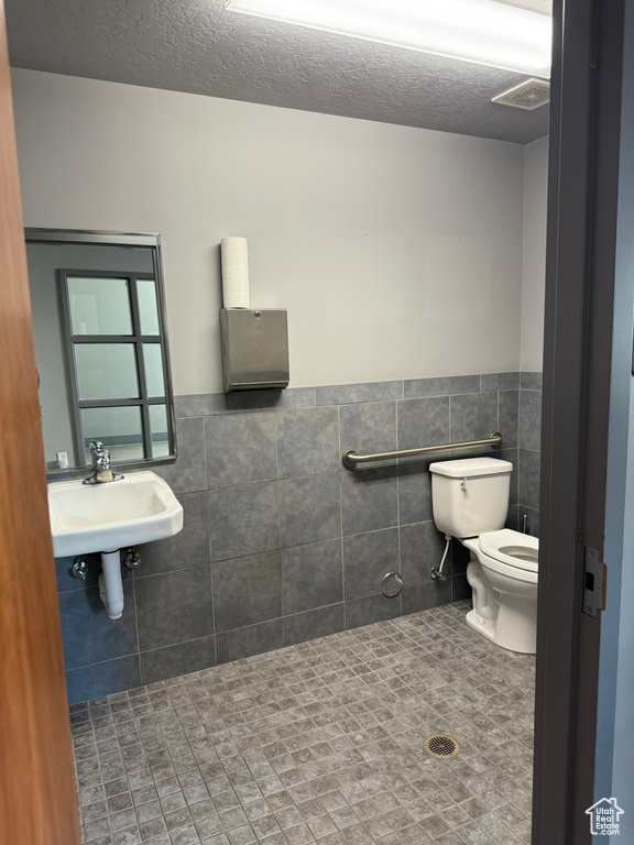 Bathroom with a sink, wainscoting, toilet, and tile walls