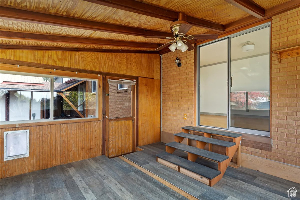 Unfurnished sunroom featuring vaulted ceiling with beams, ceiling fan, and wooden ceiling