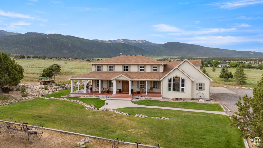 View of front facade featuring a porch, a mountain view, a front lawn, and gravel driveway