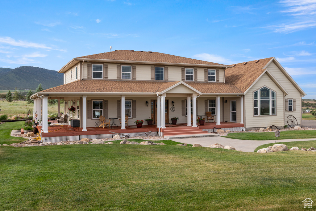 View of front of home with a porch, a front yard, a mountain view, and a shingled roof