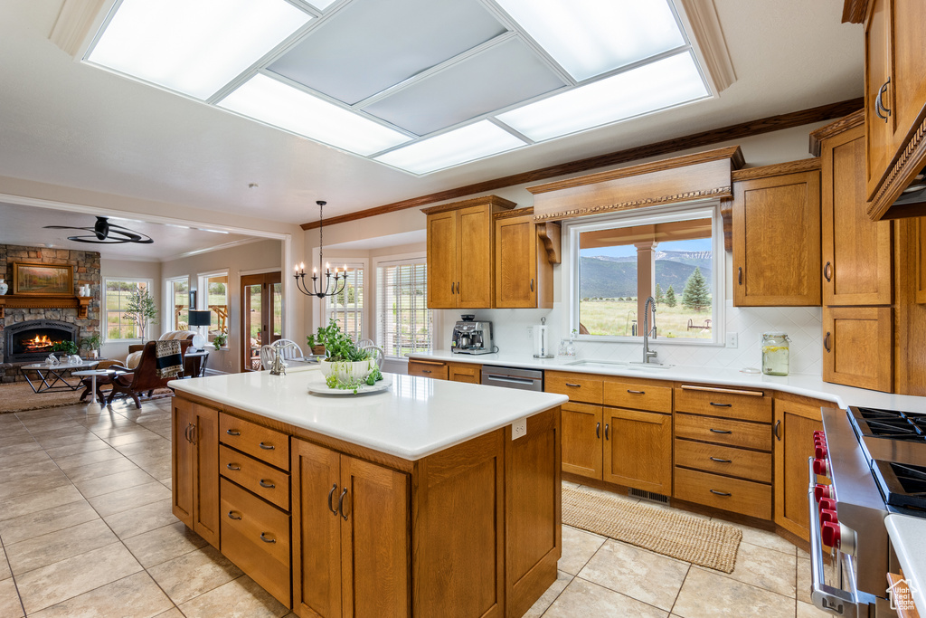 Kitchen featuring brown cabinets, a kitchen island, ceiling fan, a brick fireplace, and ornamental molding