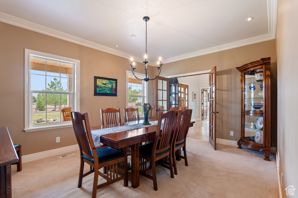Dining area featuring light colored carpet, a chandelier, and ornamental molding