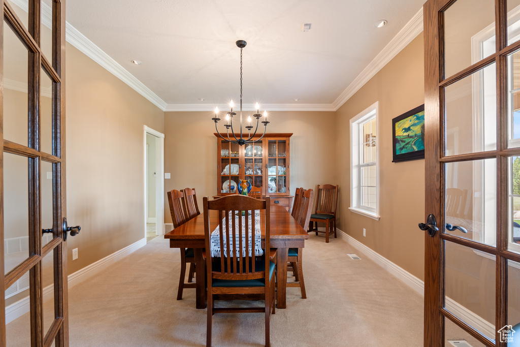 Dining space featuring french doors, a chandelier, light colored carpet, and ornamental molding