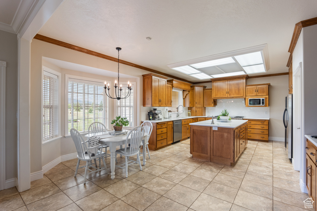 Kitchen featuring appliances with stainless steel finishes, a chandelier, crown molding, light countertops, and brown cabinets