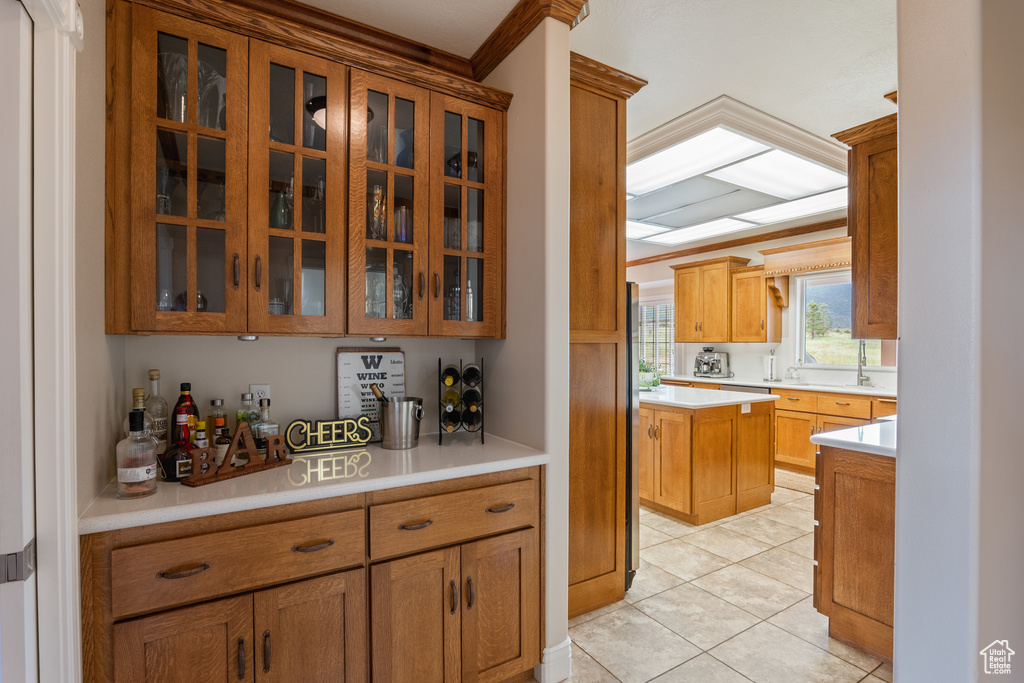 Kitchen featuring light countertops, light tile patterned floors, glass insert cabinets, and brown cabinetry