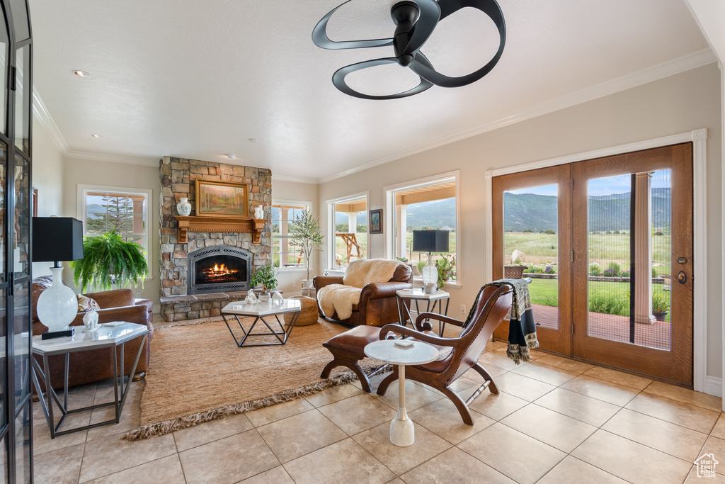 Living area with light tile patterned floors, a ceiling fan, a stone fireplace, ornamental molding, and a mountain view