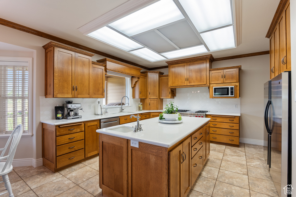 Kitchen with appliances with stainless steel finishes, brown cabinetry, light countertops, an island with sink, and crown molding