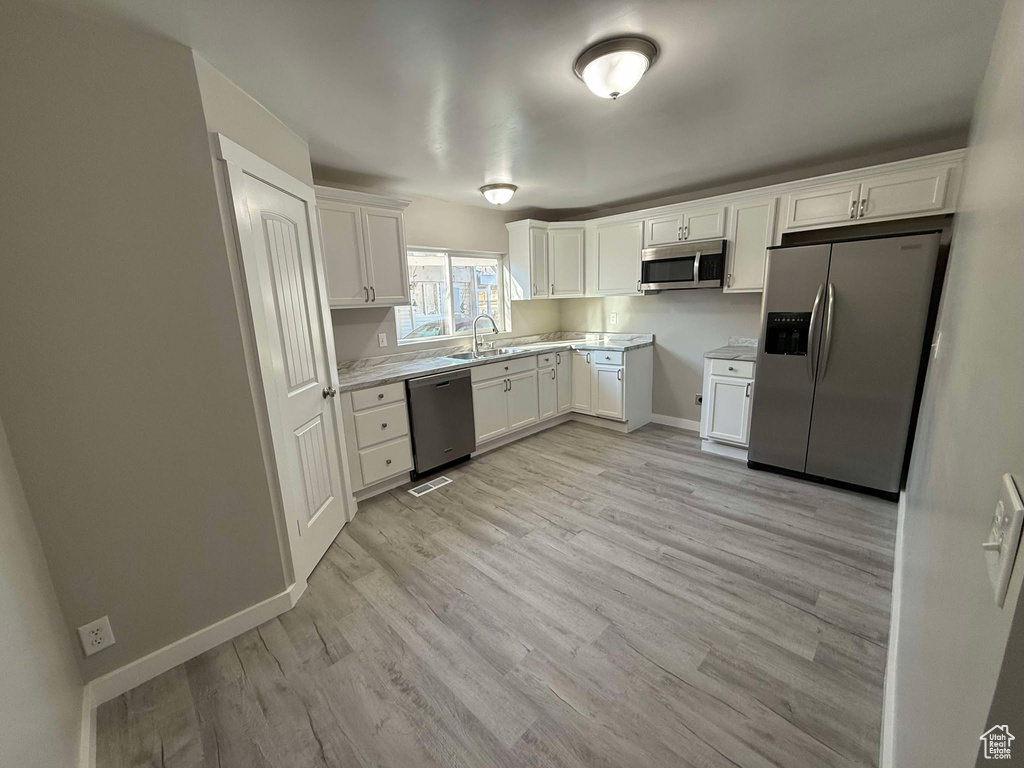 Kitchen featuring stainless steel appliances, white cabinets, sink, and light hardwood / wood-style floors