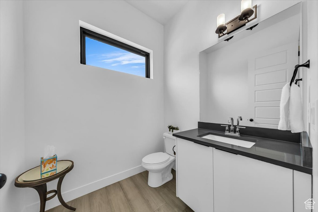 Bathroom featuring baseboards, toilet, wood finished floors, and vanity