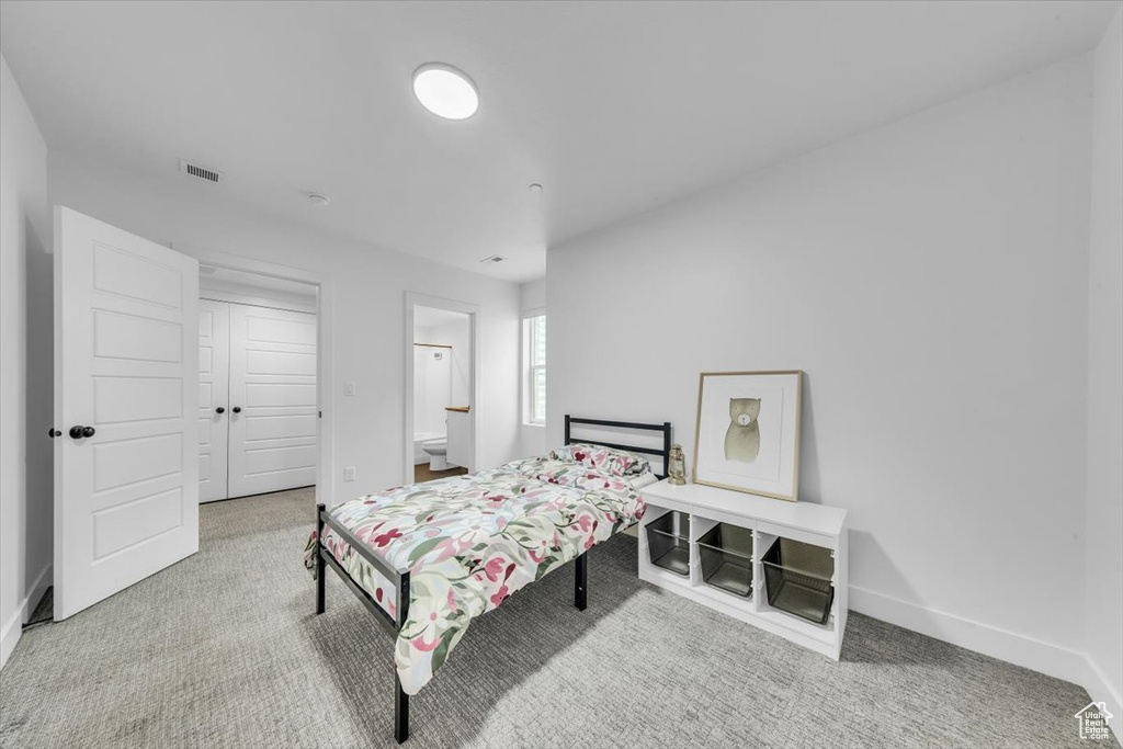 Carpeted bedroom featuring baseboards, visible vents, and ensuite bathroom