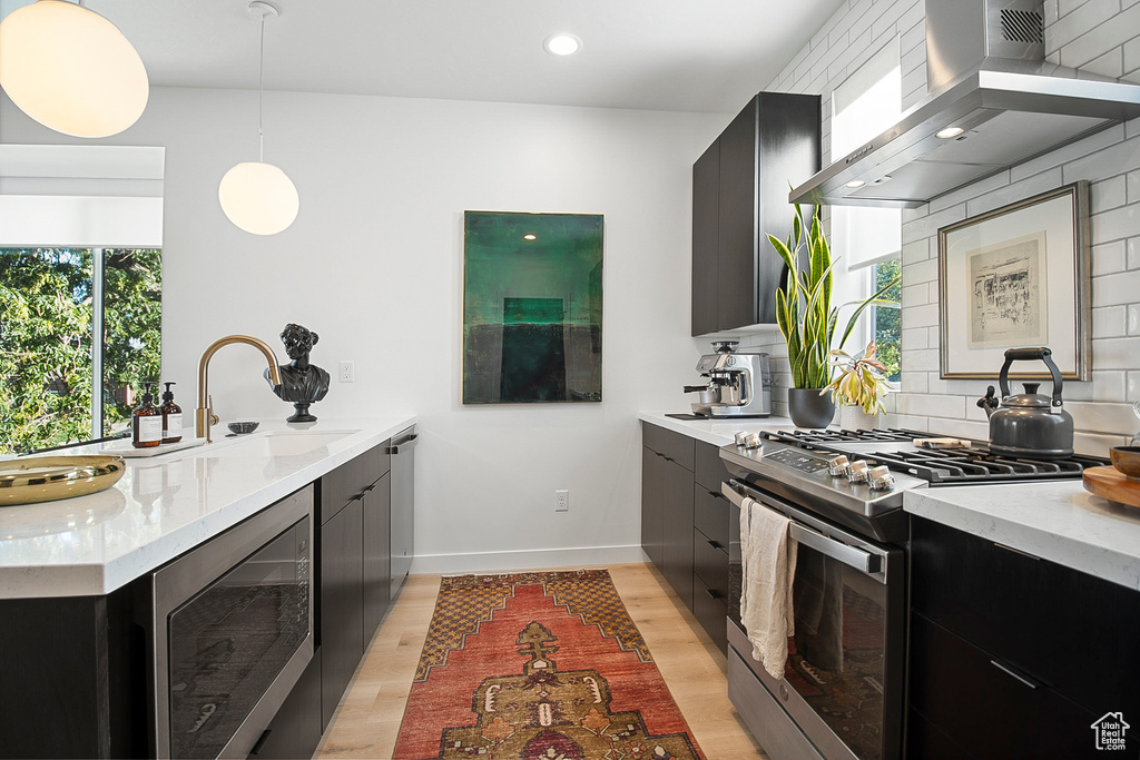 Kitchen with wall chimney exhaust hood, stainless steel appliances, wine cooler, pendant lighting, and decorative backsplash