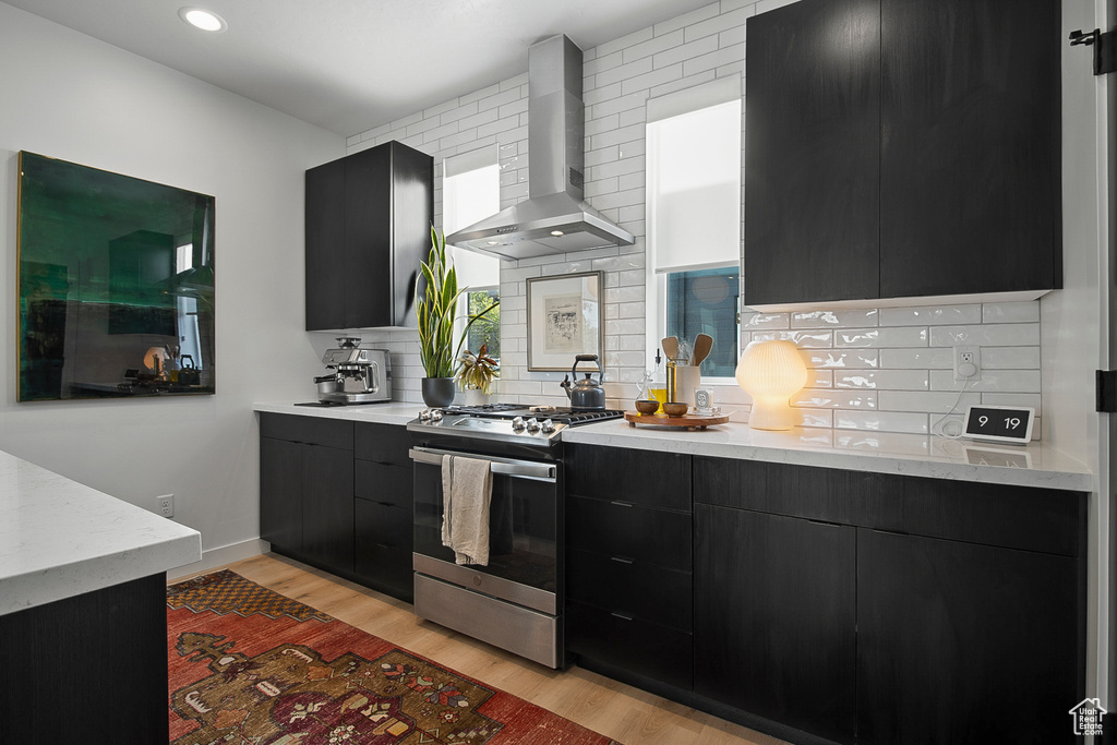 Kitchen featuring stainless steel stove, light hardwood / wood-style flooring, tasteful backsplash, and wall chimney exhaust hood