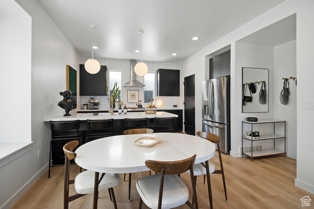 Kitchen featuring decorative light fixtures, stainless steel fridge, wall chimney range hood, and backsplash