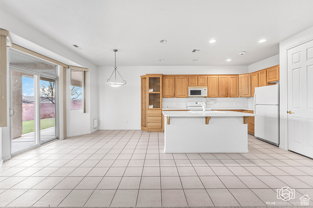 Kitchen with a breakfast bar, white appliances, light tile patterned floors, hanging light fixtures, and an island with sink