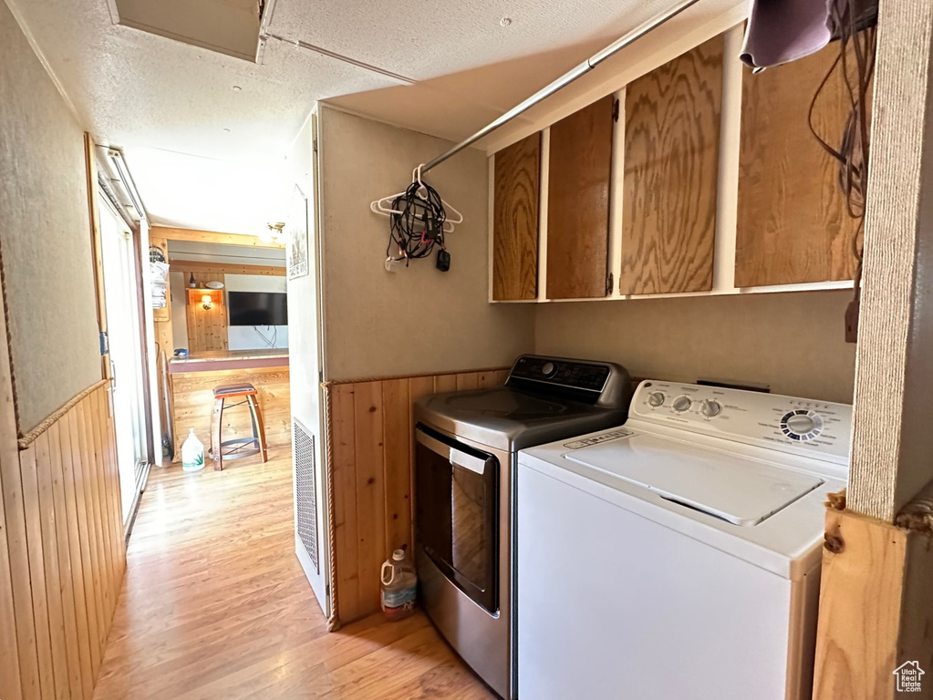 Washroom with cabinets, a textured ceiling, separate washer and dryer, light hardwood / wood-style floors, and wood walls