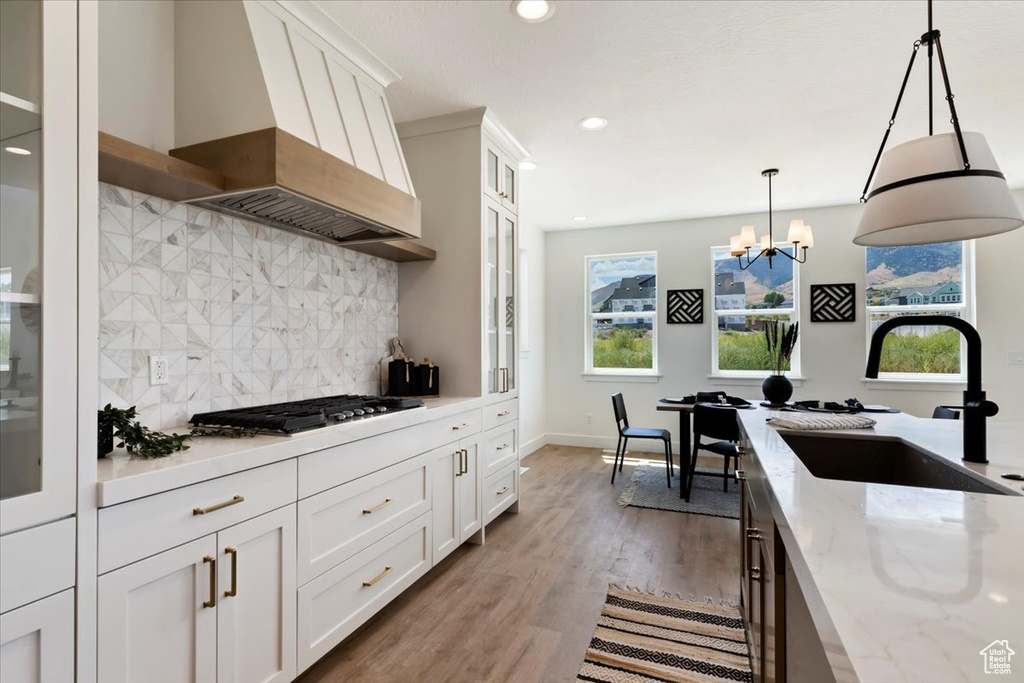 Kitchen featuring light stone counters, custom exhaust hood, stainless steel gas cooktop, sink, and white cabinets