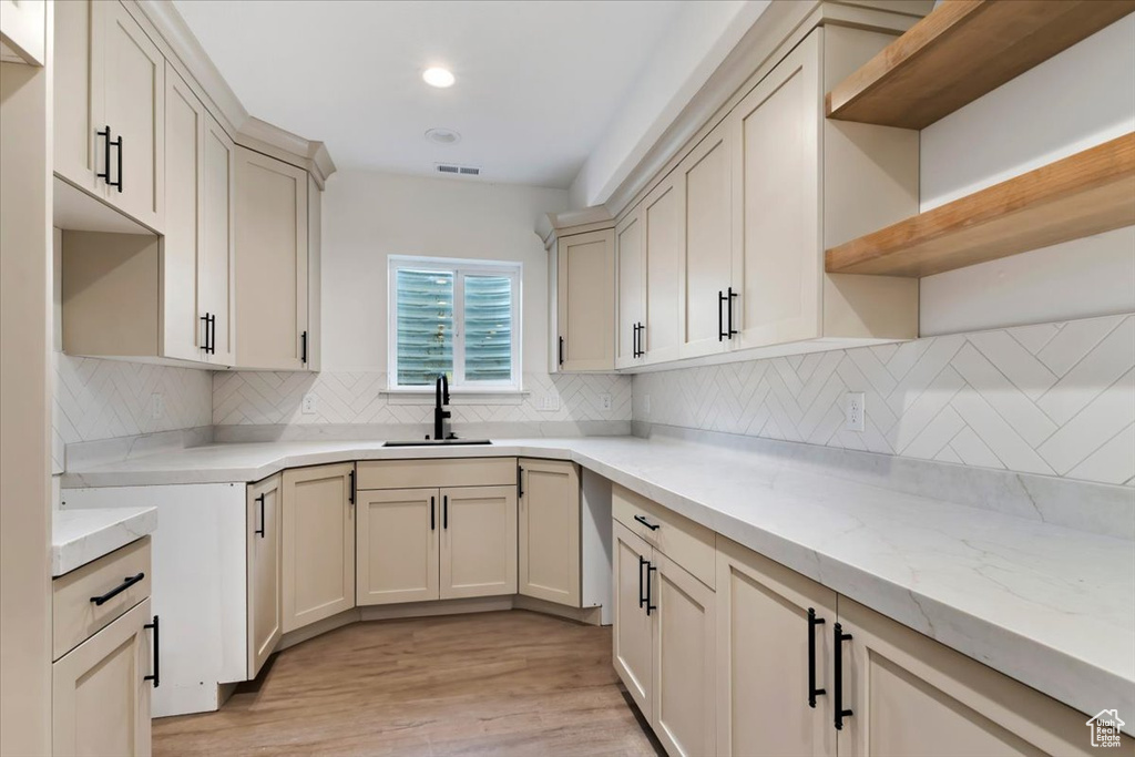 Kitchen featuring decorative backsplash, cream cabinets, sink, and light wood-type flooring