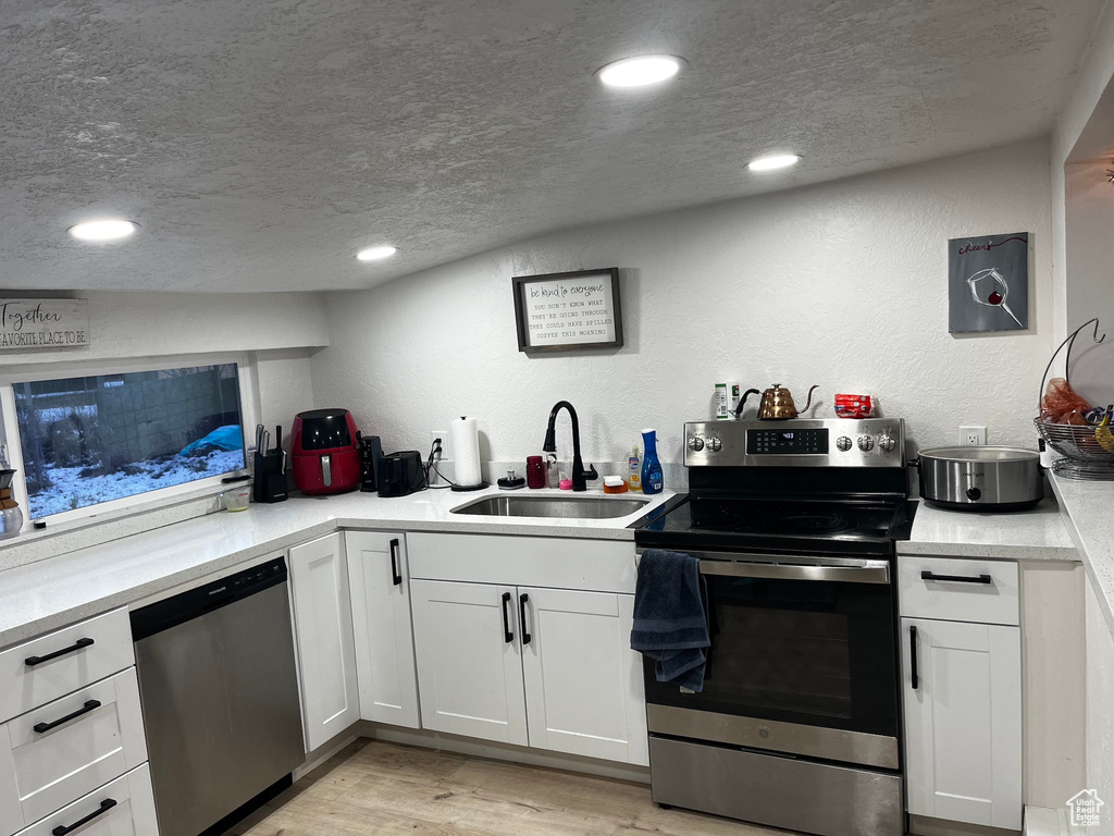 Kitchen with appliances with stainless steel finishes, light wood-type flooring, a textured ceiling, sink, and white cabinets