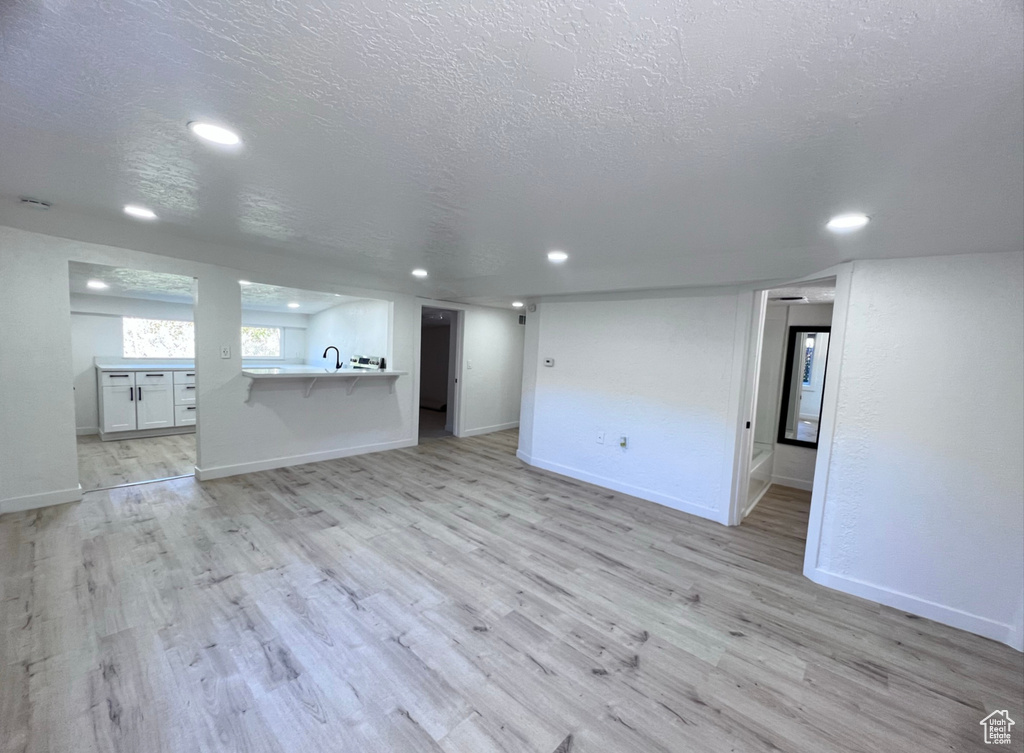 Unfurnished living room with a textured ceiling, light hardwood / wood-style floors, and sink