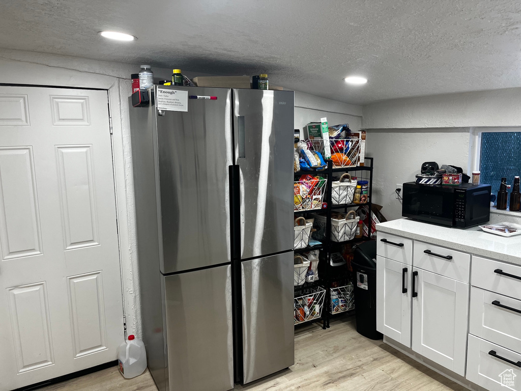 Kitchen with light wood-type flooring, stainless steel fridge, a textured ceiling, and white cabinetry