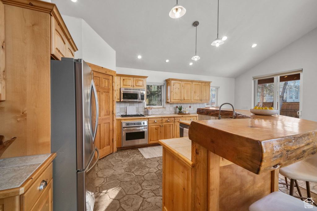 Kitchen with an island with sink, appliances with stainless steel finishes, tasteful backsplash, vaulted ceiling, and pendant lighting