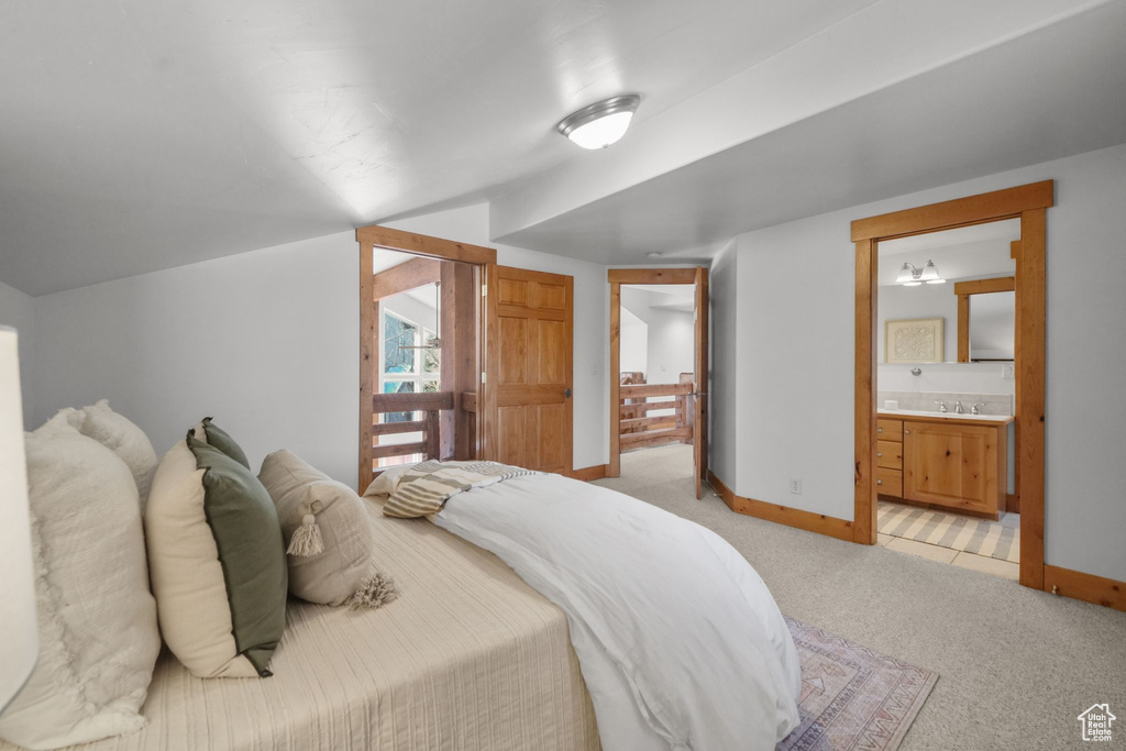 Bedroom featuring light carpet, vaulted ceiling, connected bathroom, and sink