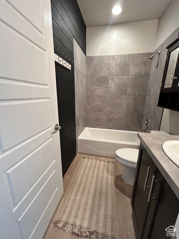 Full bathroom featuring tiled shower / bath combo, vanity, wood-type flooring, toilet, and wood walls