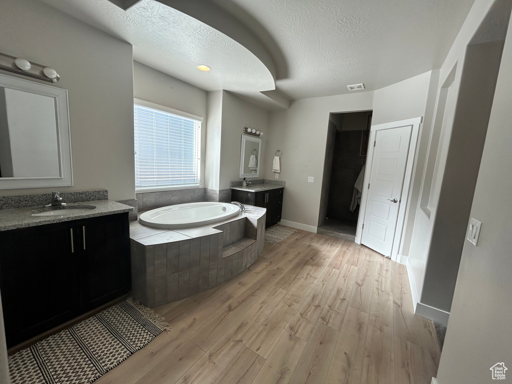 Bathroom featuring vanity, hardwood / wood-style floors, a relaxing tiled tub, and a textured ceiling