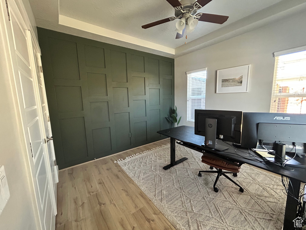 Office area with ceiling fan, a raised ceiling, and light wood-type flooring